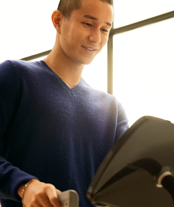 Young man smiling while holding a tablet and smartphone near a large window.